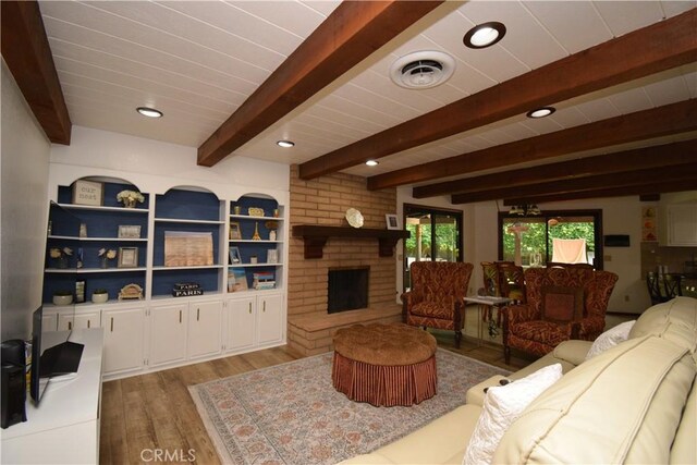 living room featuring beam ceiling, light hardwood / wood-style floors, and a brick fireplace