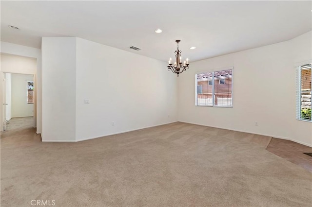 spare room with light colored carpet and a notable chandelier