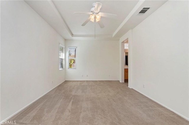 carpeted spare room featuring a tray ceiling and ceiling fan