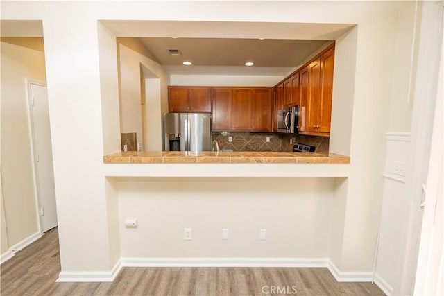 kitchen featuring backsplash, kitchen peninsula, light hardwood / wood-style flooring, and appliances with stainless steel finishes