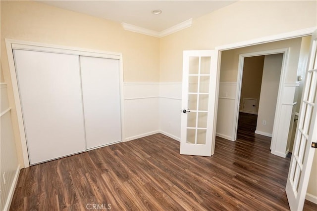 unfurnished bedroom featuring a closet, french doors, crown molding, and dark hardwood / wood-style floors