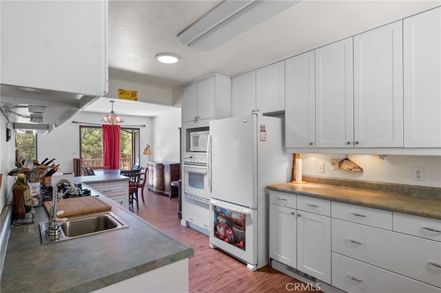 kitchen with hanging light fixtures, white cabinetry, light hardwood / wood-style flooring, sink, and white appliances