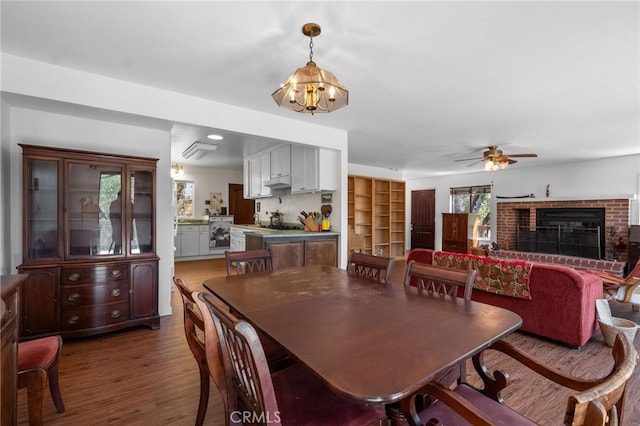 dining room with ceiling fan with notable chandelier, a healthy amount of sunlight, dark wood-type flooring, and a fireplace