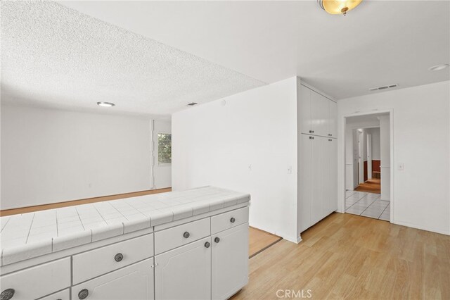 interior space with white cabinets, a textured ceiling, light wood-type flooring, and tile counters