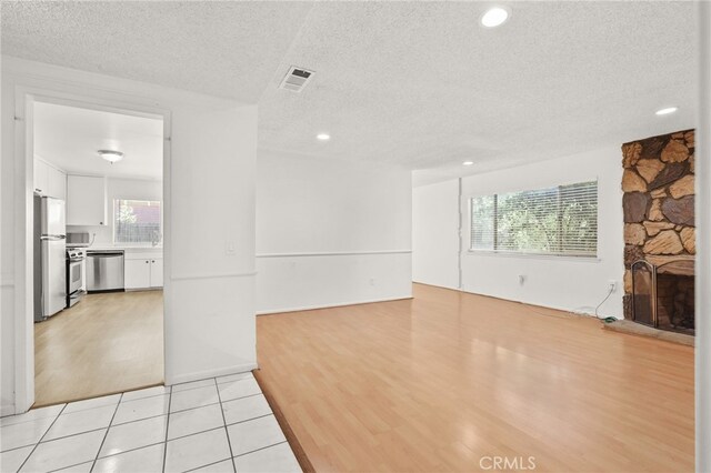 unfurnished living room with a fireplace, a textured ceiling, a wealth of natural light, and light tile patterned flooring