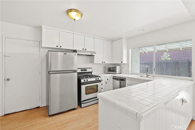 kitchen with tile countertops, kitchen peninsula, light hardwood / wood-style floors, white cabinets, and appliances with stainless steel finishes