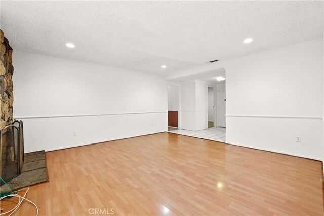 unfurnished living room with a stone fireplace, light wood-type flooring, and a textured ceiling