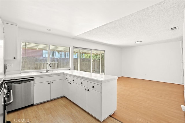 kitchen with light wood-type flooring, stainless steel dishwasher, sink, tile countertops, and white cabinets