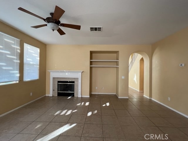 unfurnished living room with built in shelves, tile patterned flooring, ceiling fan, and a tiled fireplace