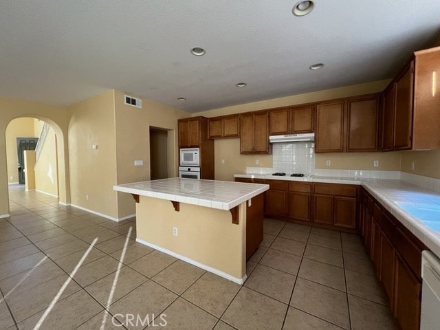 kitchen featuring a kitchen breakfast bar, decorative backsplash, white appliances, light tile patterned floors, and tile countertops