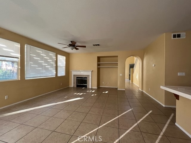 unfurnished living room featuring built in shelves, ceiling fan, and tile patterned floors