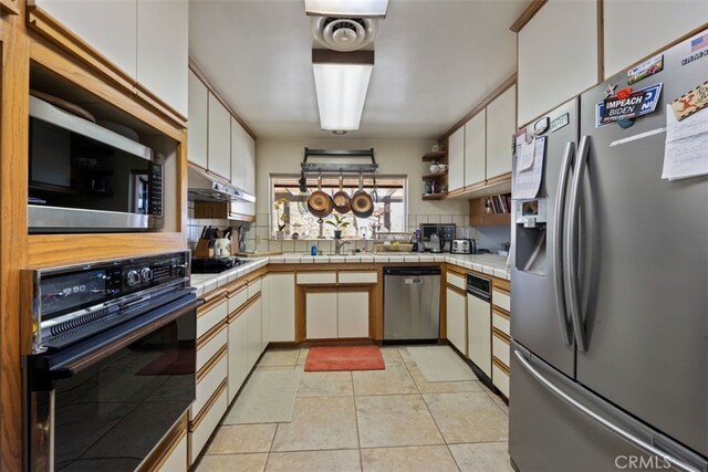 kitchen featuring light tile patterned flooring, tasteful backsplash, white cabinets, black appliances, and tile counters