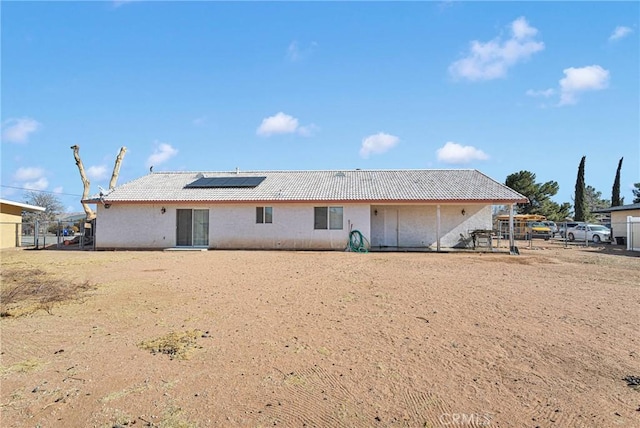 rear view of house featuring roof mounted solar panels, fence, and a tiled roof