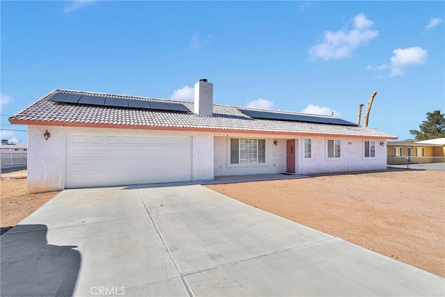 ranch-style home featuring a tile roof, a chimney, driveway, an attached garage, and solar panels