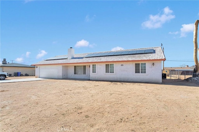 rear view of property featuring a garage and solar panels