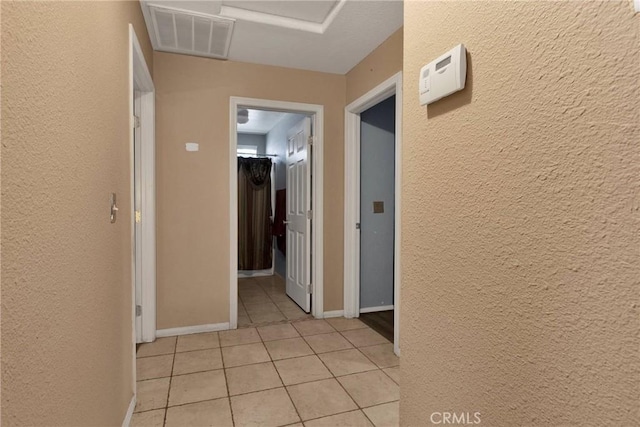 hallway with a textured wall, baseboards, visible vents, and light tile patterned flooring
