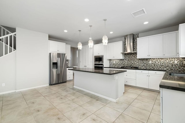 kitchen with white cabinets, a kitchen island, appliances with stainless steel finishes, wall chimney exhaust hood, and decorative light fixtures