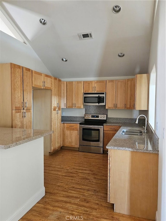 kitchen with sink, vaulted ceiling, light stone counters, dark hardwood / wood-style flooring, and stainless steel appliances