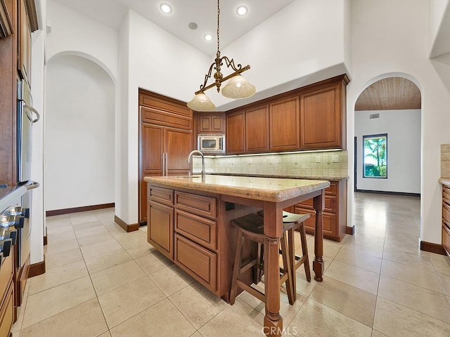 kitchen featuring light stone countertops, built in appliances, high vaulted ceiling, hanging light fixtures, and an island with sink