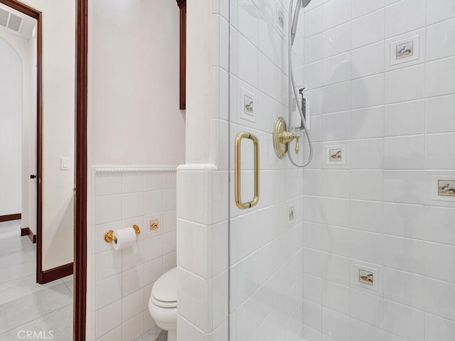 bathroom featuring tile patterned flooring, toilet, a shower with shower door, and tile walls