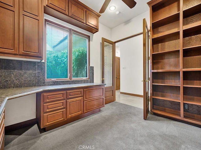 unfurnished office featuring built in desk, light colored carpet, and ceiling fan