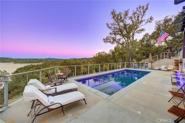 pool at dusk with a patio area and a water view