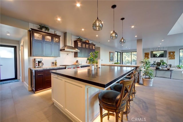 kitchen featuring tasteful backsplash, a kitchen breakfast bar, hanging light fixtures, a center island, and wall chimney exhaust hood