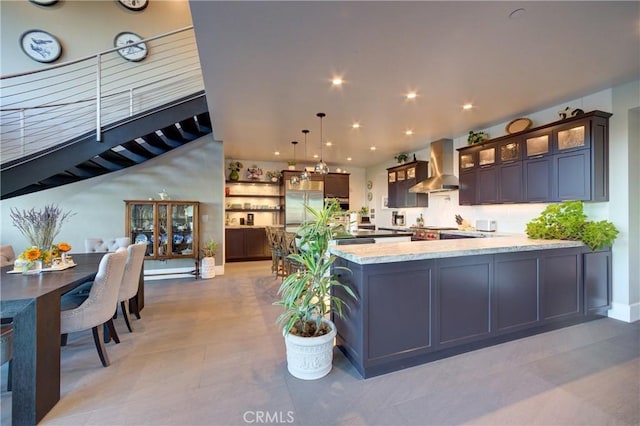 kitchen featuring hanging light fixtures, stainless steel built in refrigerator, light stone countertops, kitchen peninsula, and wall chimney exhaust hood