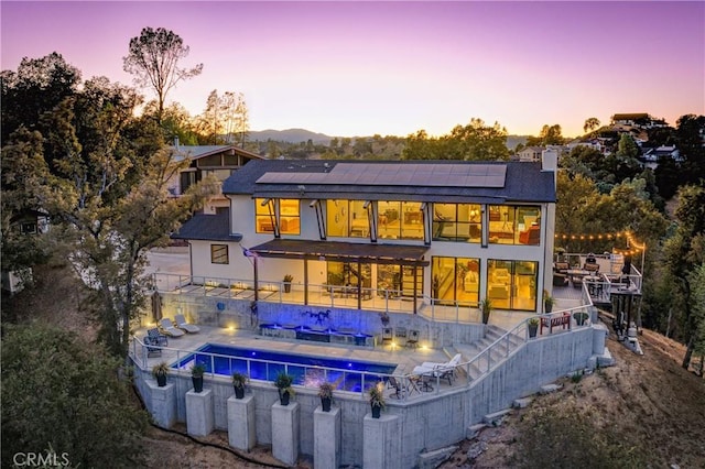 back house at dusk with a patio and solar panels