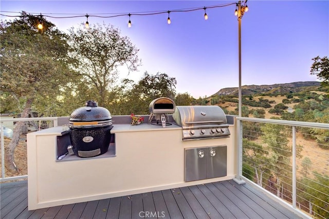 deck at dusk with a mountain view, an outdoor kitchen, and grilling area