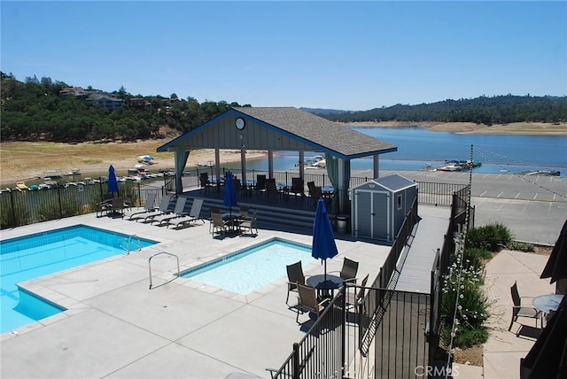 view of swimming pool featuring a water view, a patio, a shed, and a gazebo