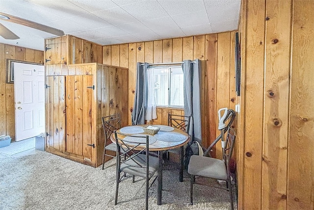 carpeted dining area with ceiling fan and wood walls