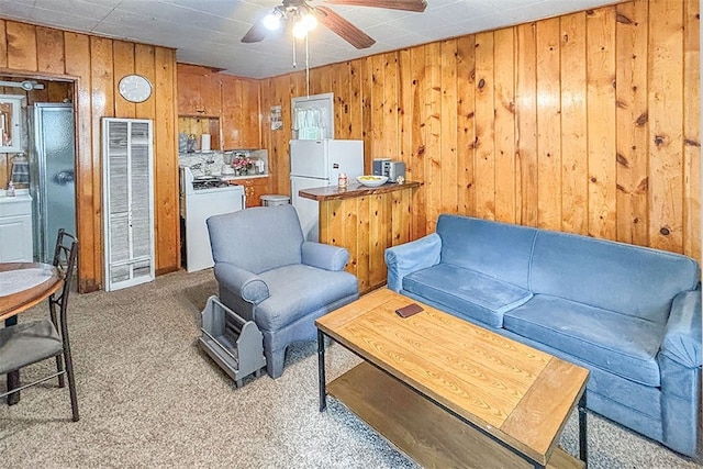 carpeted living room featuring wooden walls and ceiling fan