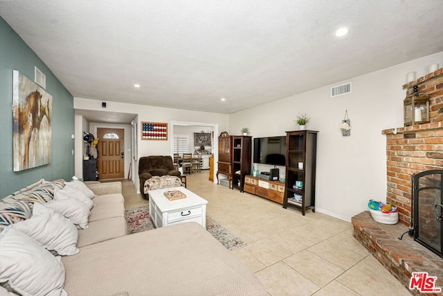 living room with a textured ceiling, light tile patterned flooring, and a brick fireplace