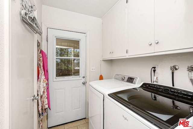 washroom with washing machine and dryer, light tile patterned flooring, and cabinets