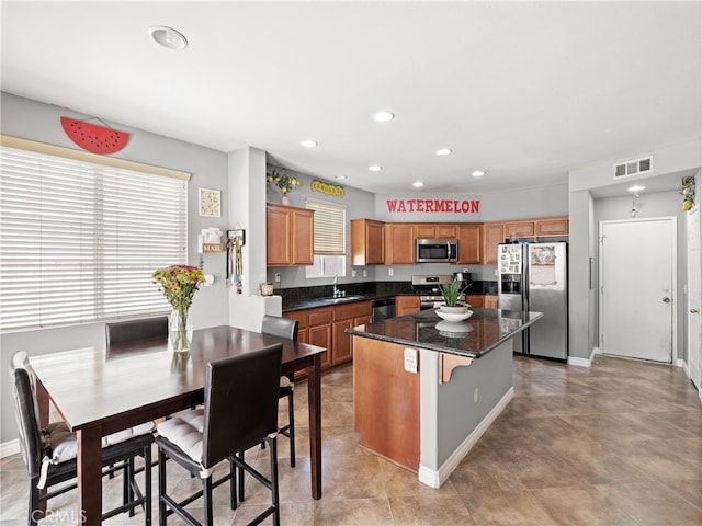 kitchen featuring sink, stainless steel appliances, a center island, dark stone counters, and a kitchen bar