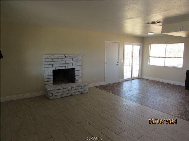 unfurnished living room featuring wood-type flooring and a brick fireplace