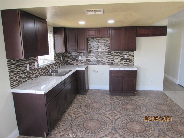 kitchen featuring dark brown cabinetry, tile countertops, tasteful backsplash, and sink