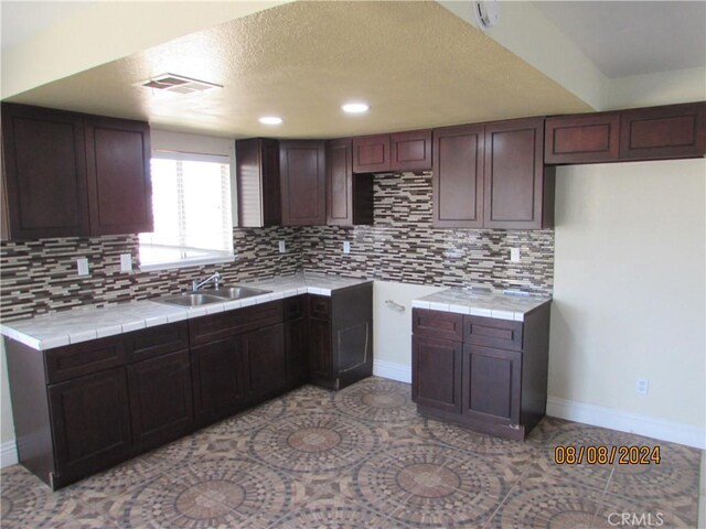 kitchen featuring decorative backsplash, dark brown cabinets, tile countertops, and sink