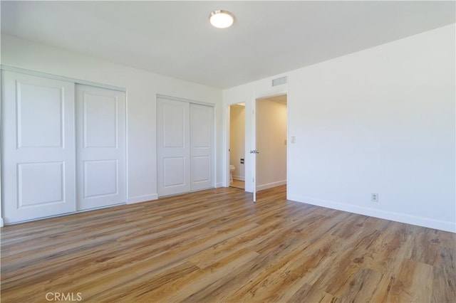 unfurnished bedroom featuring light hardwood / wood-style flooring and multiple closets