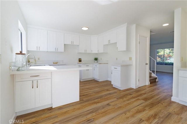 kitchen featuring kitchen peninsula, white cabinetry, light hardwood / wood-style flooring, and sink