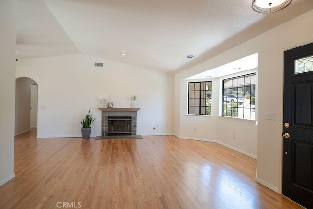 unfurnished living room with vaulted ceiling, light wood-type flooring, and a fireplace