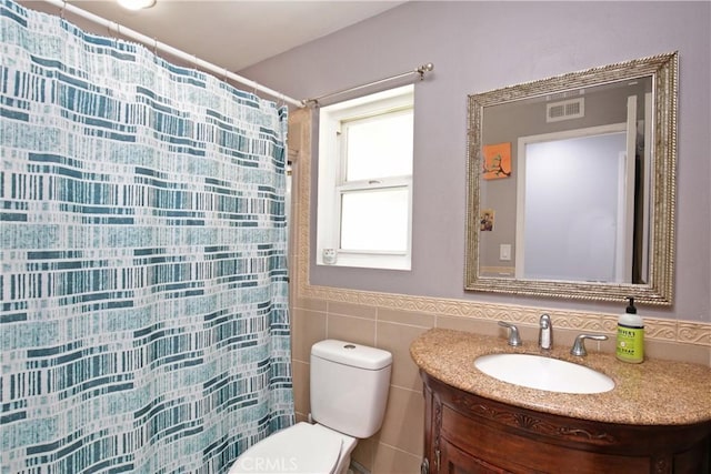 bathroom featuring vanity, tile walls, and toilet