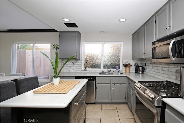 kitchen with sink, light tile patterned floors, appliances with stainless steel finishes, gray cabinets, and backsplash