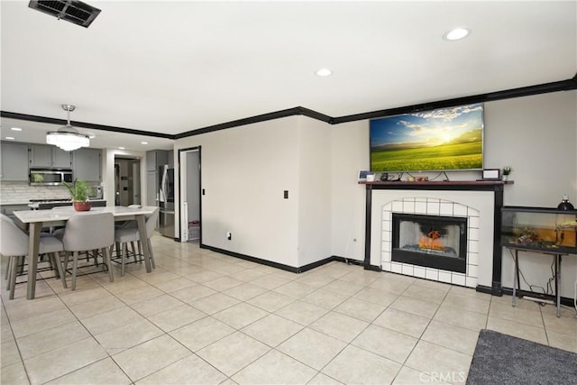 living room with a tiled fireplace, crown molding, and light tile patterned flooring