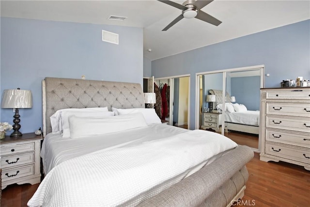 bedroom featuring lofted ceiling, two closets, dark hardwood / wood-style floors, and ceiling fan