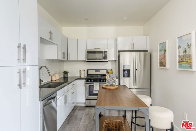 kitchen with appliances with stainless steel finishes, white cabinetry, tasteful backsplash, hardwood / wood-style floors, and sink