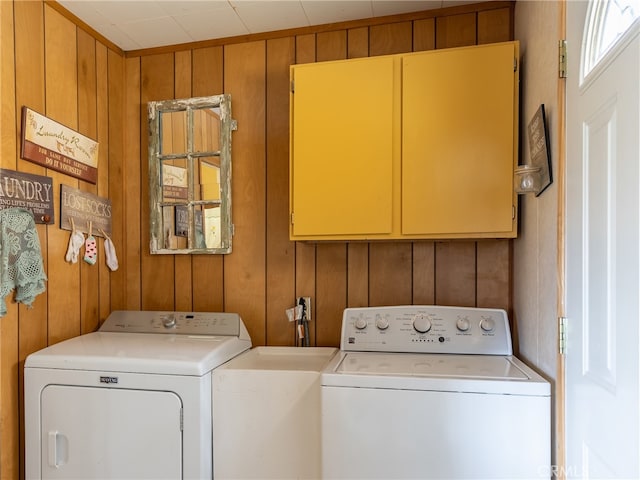 laundry area featuring cabinets, wooden walls, and separate washer and dryer