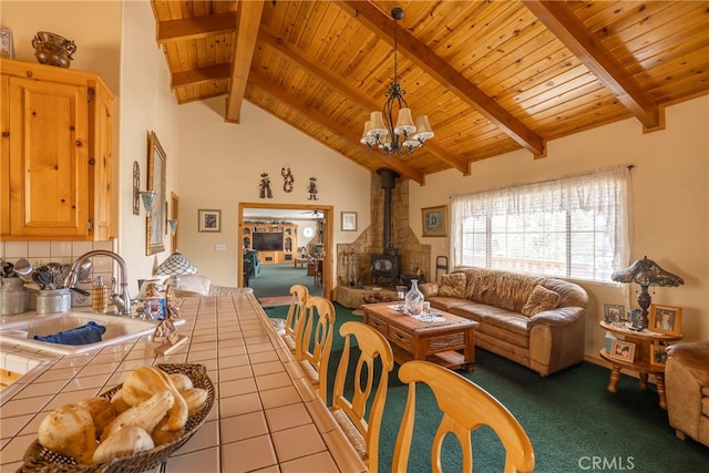 dining space with beam ceiling, a wood stove, sink, light tile patterned flooring, and an inviting chandelier