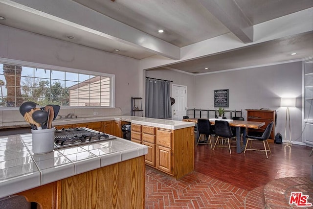 kitchen with beamed ceiling, crown molding, stainless steel gas stovetop, and tile counters